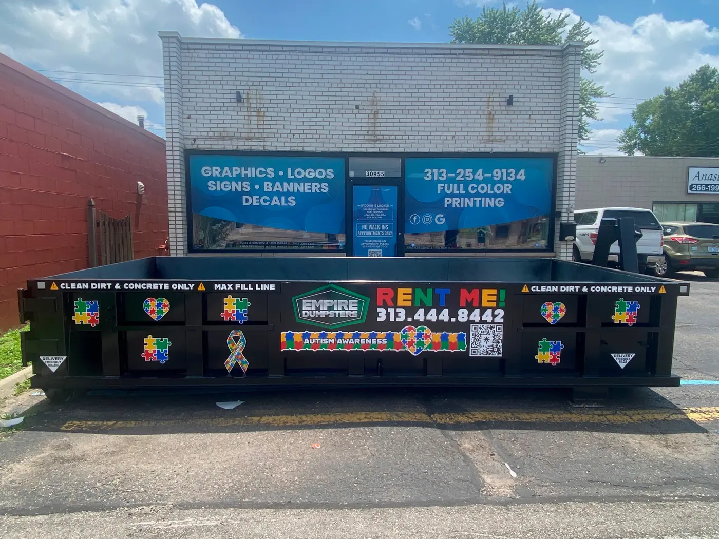Empire Dumpsters roll-off dumpster with autism-awareness puzzle-piece hearts and ribbon graphics