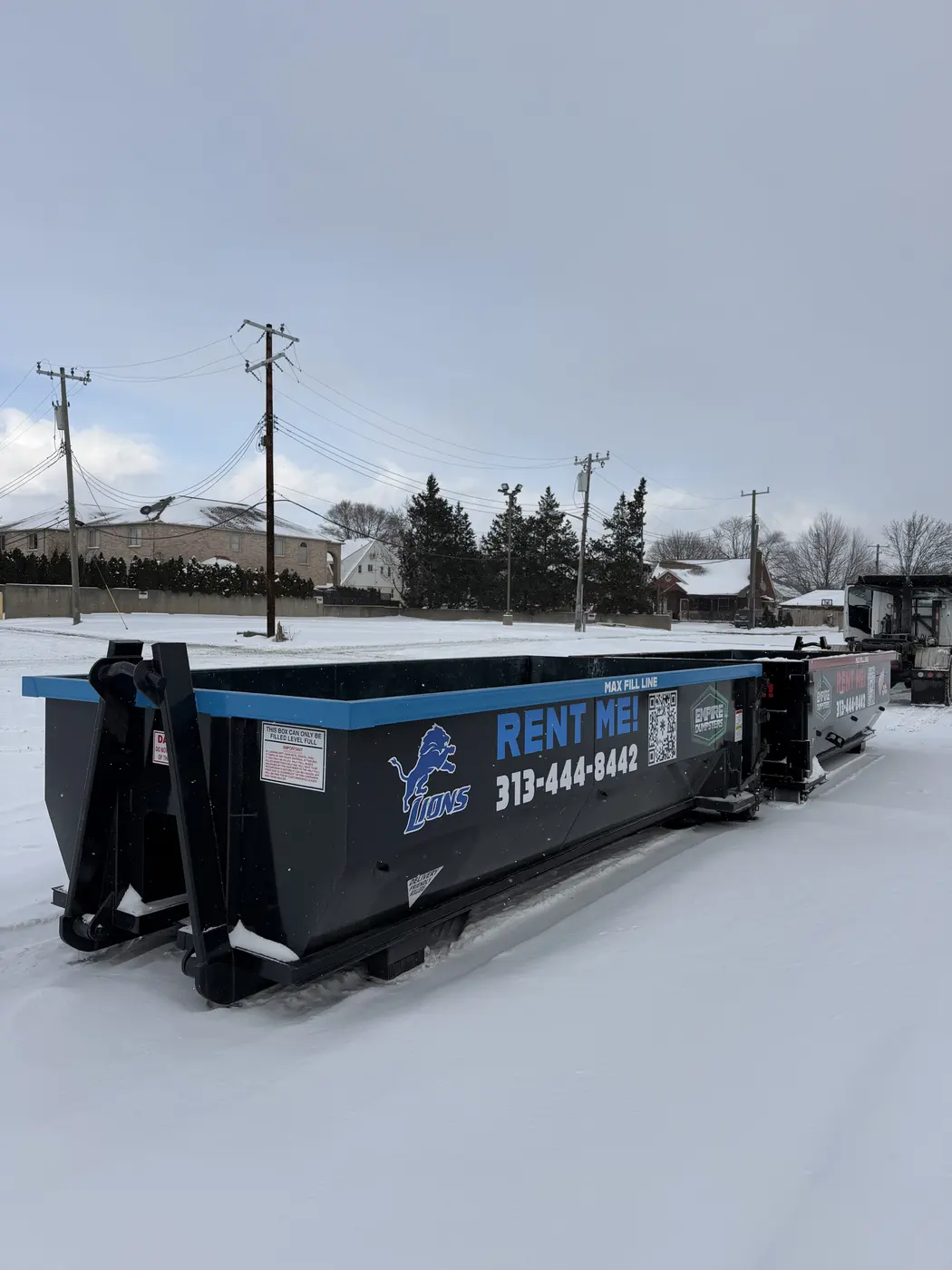 Empire Dumpsters roll-off dumpster wrapped in Detroit Lions blue with the Lions logo, sitting in fresh snow