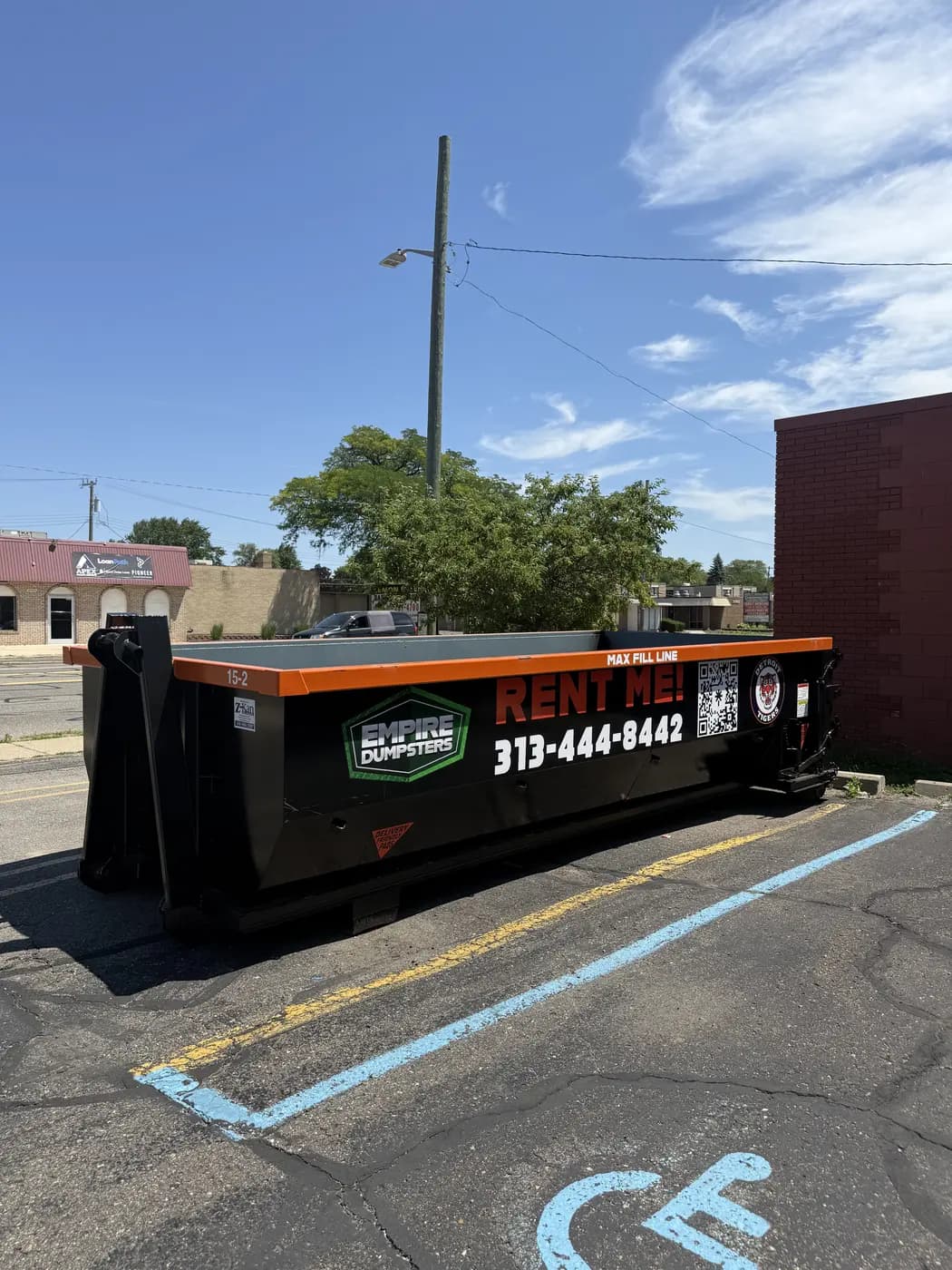 Empire Dumpsters roll-off with an orange rail and a Detroit Tigers logo under a blue sky